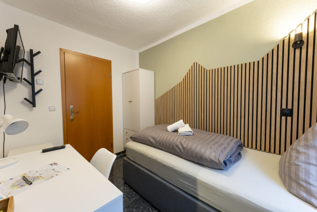 Blick in Zimmer 6, Einzelzimmer mit Boxspringbett, Schreibtisch und Kleiderschrank