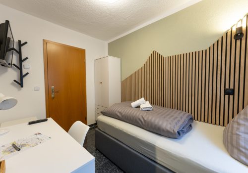 Blick in Zimmer 6, Einzelzimmer mit Boxspringbett, Schreibtisch und Kleiderschrank